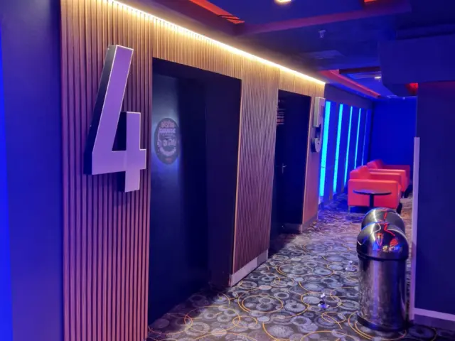 Numerele volumetrice 4 și 5 marchează intrările sălilor într-un coridor iluminat albastru și roșu.