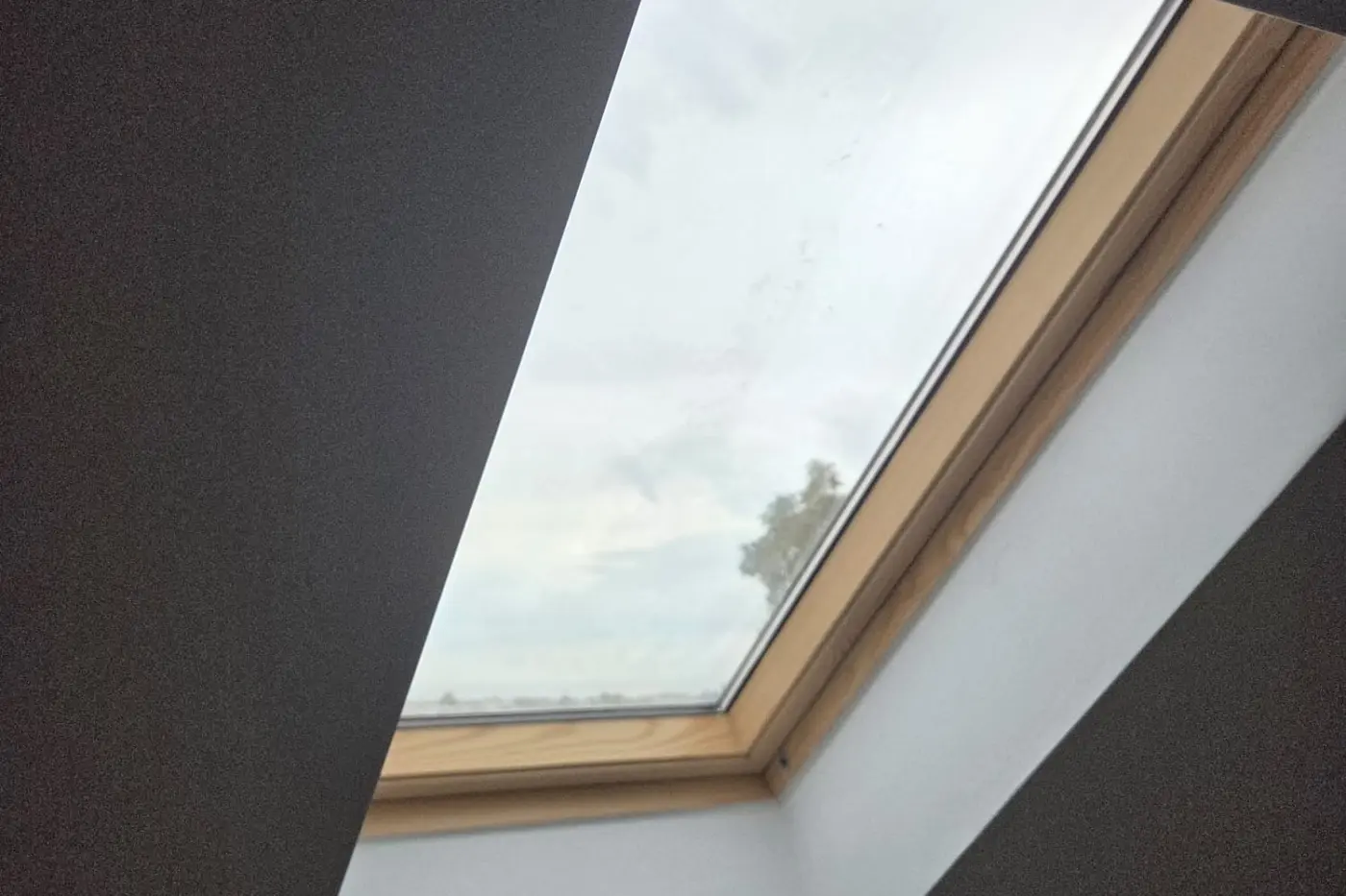 Fereastră de mansardă tratată cu folie de protecție solară, văzută din interiorul unei încăperi.
