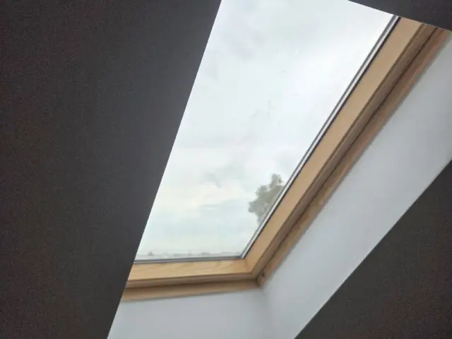 Fereastră de mansardă tratată cu folie de protecție solară, văzută din interiorul unei încăperi.