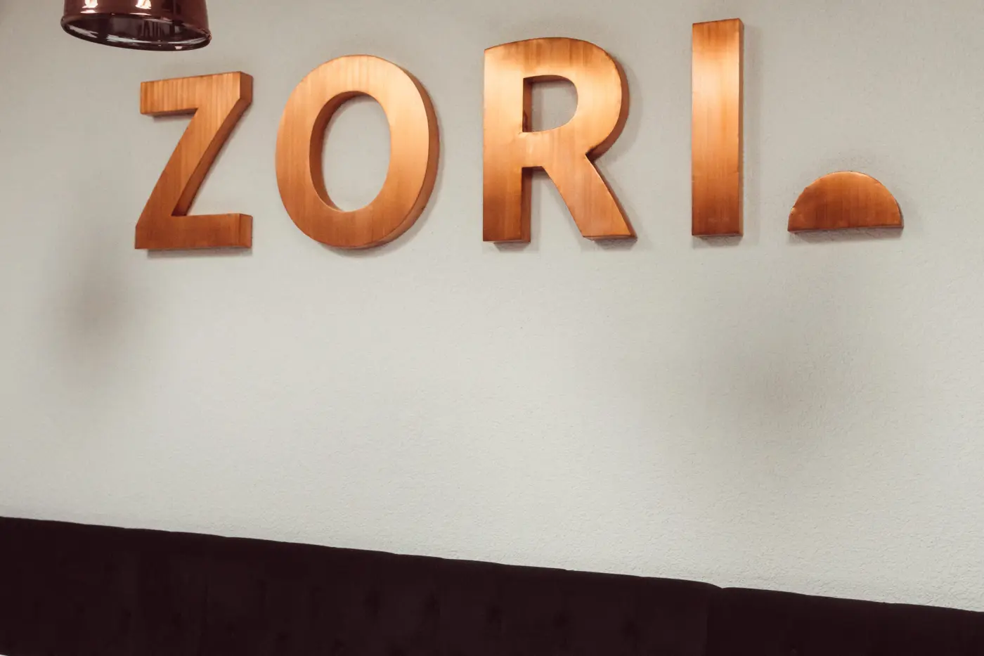 Litere volumetrice ZORI cu finisaj arămiu, montate pe perete deasupra meselor unui restaurant.
