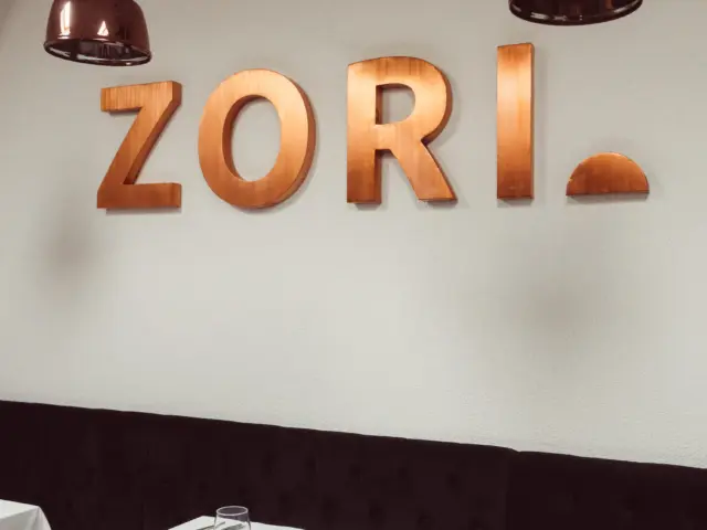 Litere volumetrice ZORI cu finisaj arămiu, montate pe perete deasupra meselor unui restaurant.