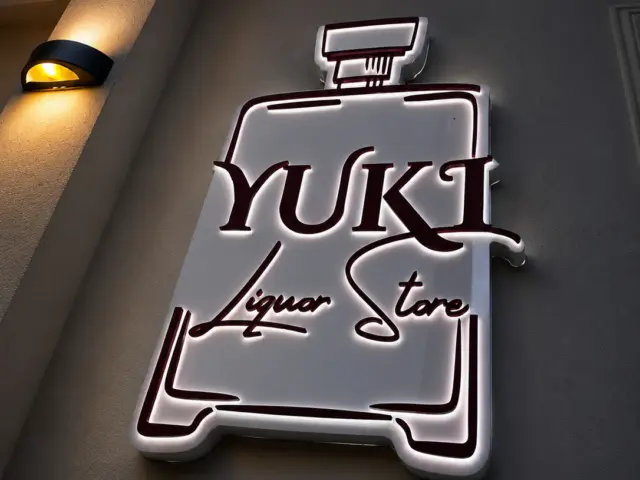 Bottle-shaped YUKI Liquor Store illuminated sign mounted on an exterior wall at dusk.