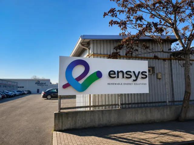 Panou Ensys cu simbol colorat și litere volumetrice, montat la exteriorul unei clădiri industriale.