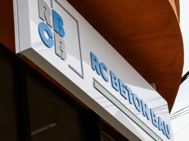 Panou exterior RC Beton Bau cu litere volumetrice albastre, montat deasupra vitrinei clădirii.