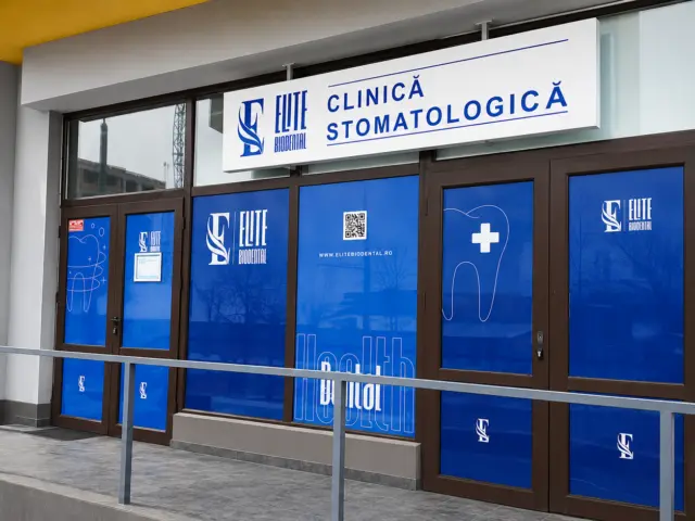 Firmă albă Elite Biodental montată deasupra intrării, pe fațada cu vitrine albastre a clinicii stomatologice.