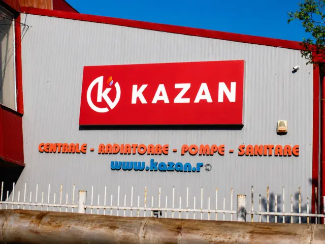 Panou roșu Kazan cu siglă și litere albe, montat pe fațada unei clădiri comerciale.