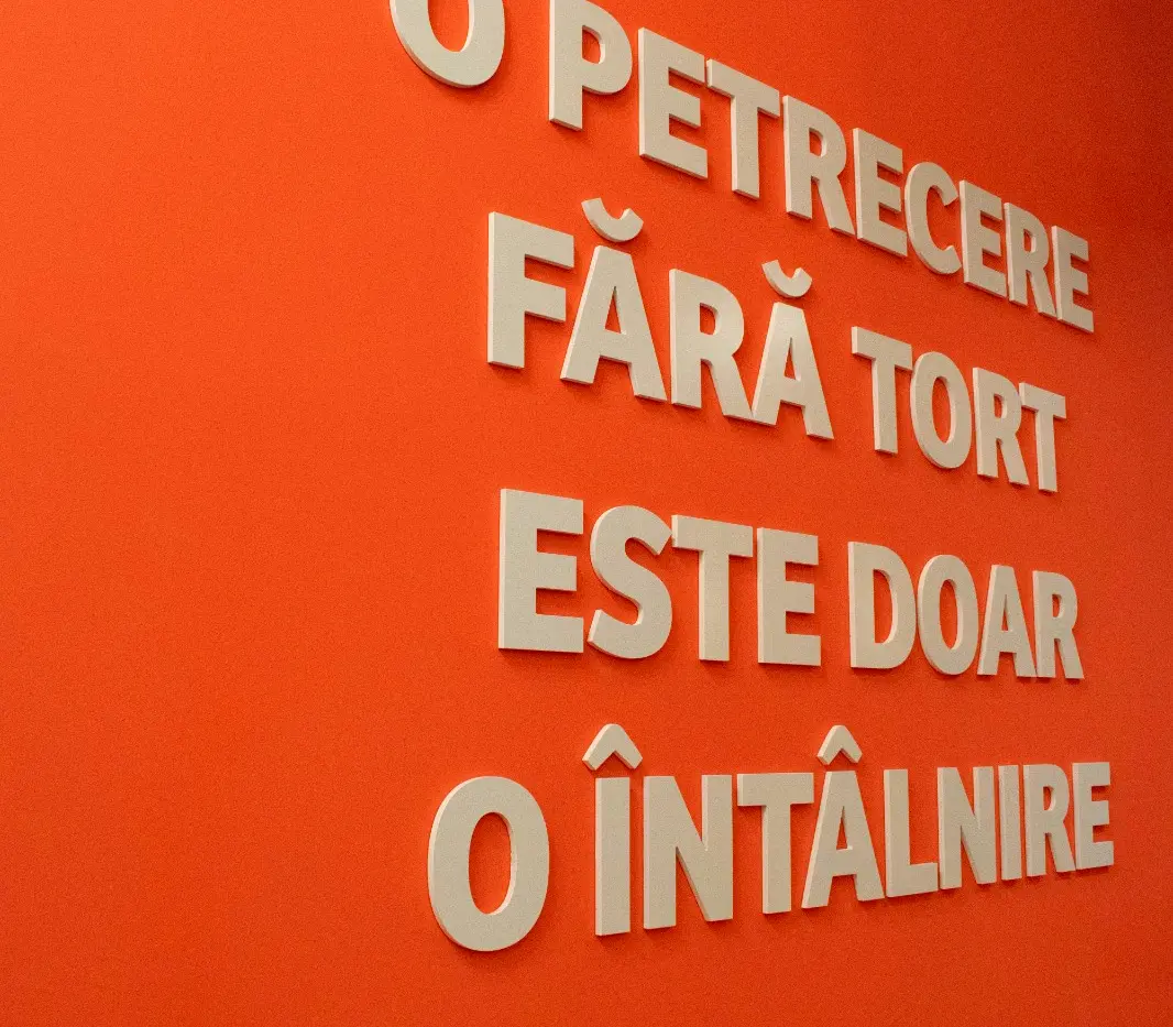Litere 3D albe dispuse pe un perete portocaliu, formând un mesaj despre petreceri și tort.