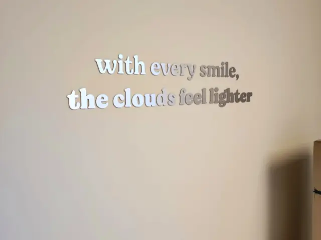 Mesajul „with every smile, the clouds feel lighter” din litere metalice, montat pe peretele unei clinici.