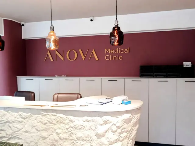 Litere volumetrice aurii ANOVA Medical Clinic, montate pe peretele vișiniu din zona de recepție.
