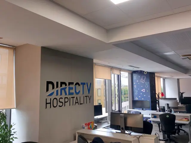 Sigla DIRECTV Hospitality din litere volumetrice, montată pe un perete despărțitor într-un birou deschis.
