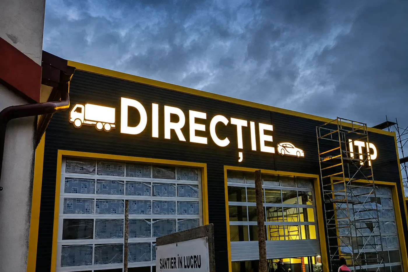 Litere luminoase „DIRECȚIE” și „ITP”, cu pictograme auto, montate pe fațada unei stații de inspecție.