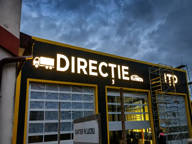 Litere luminoase „DIRECȚIE” și „ITP”, cu pictograme auto, montate pe fațada unei stații de inspecție.