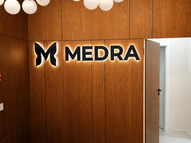 Sigla și literele luminoase MEDRA pe un perete interior placat cu lemn.