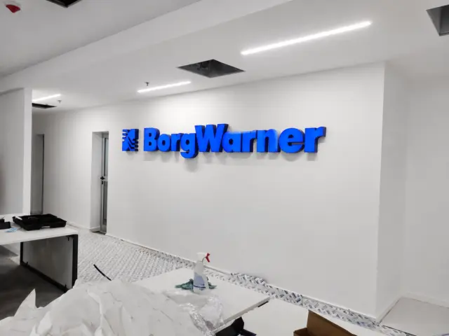 Sigla BorgWarner din litere volumetrice albastre, montată pe un perete alb într-un interior în curs de amenajare.