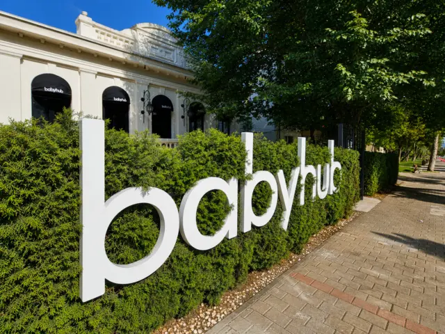 Litere volumetrice albe Babyhub amplasate pe un gard viu, lângă o alee pavată.