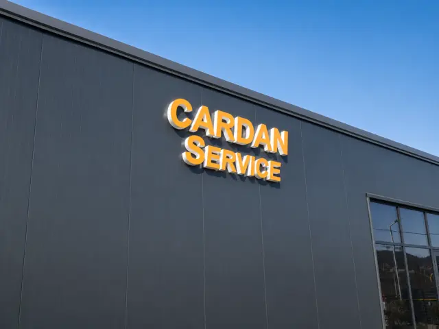 Litere volumetrice luminoase Cardan Service, cu fețe portocalii, montate pe fațada gri a clădirii.