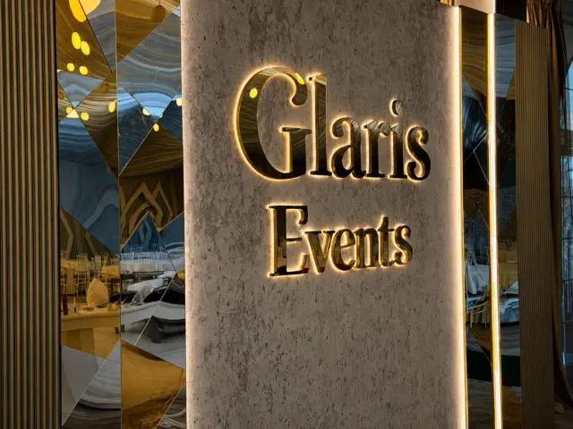 Însemnul Glaris Events cu litere reflectante iluminate din spate, montat între panouri decorative cu oglinzi.