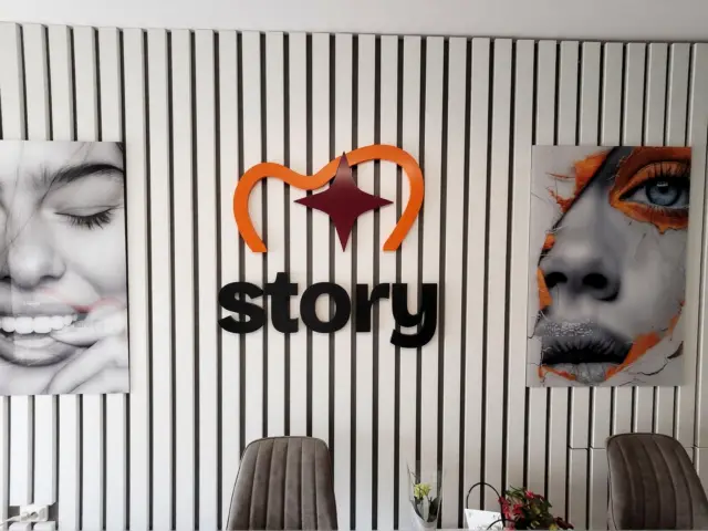 Logo și litere volumetrice Dental Story montate pe peretele lamelar al recepției, între două portrete.