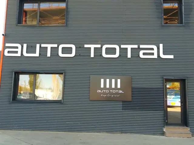 Litere volumetrice albe Auto Total montate pe fațada metalică închisă la culoare a clădirii.