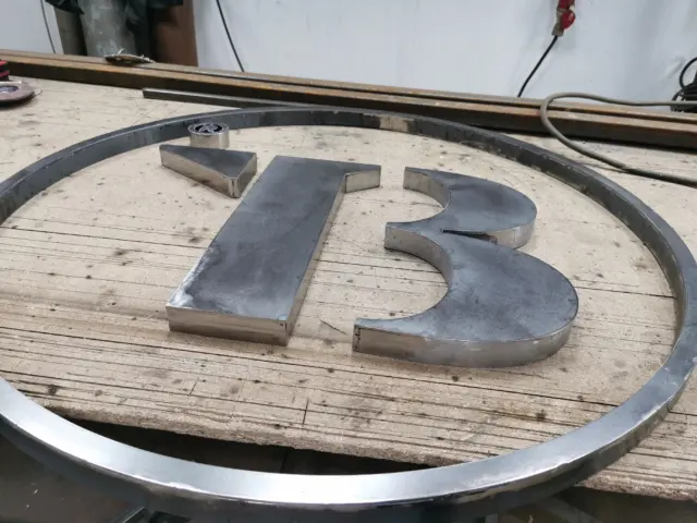 Elemente volumetrice metalice formând numărul 13, așezate într-un cadru circular pe masa de lucru.