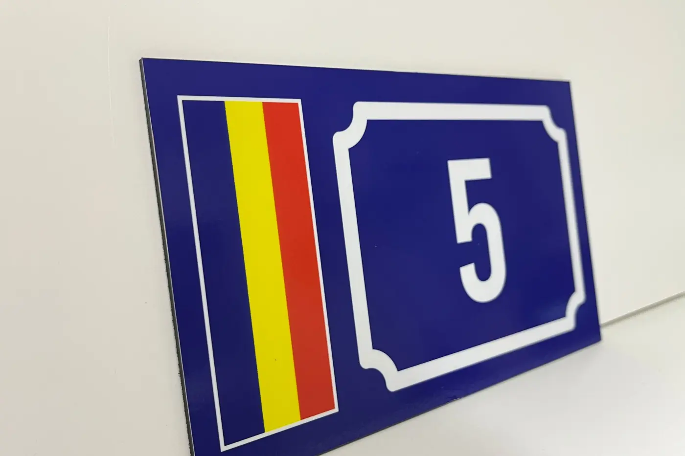 Plăcuță albastră pentru locuința cu numărul 5, decorată cu drapelul României și așezată pe o suprafață albă.