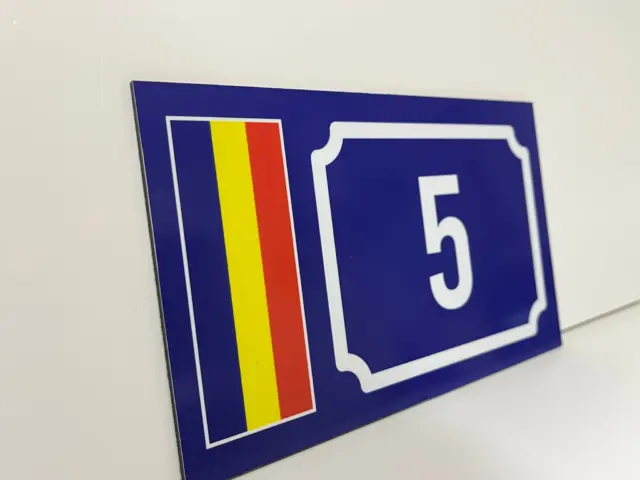 Plăcuță albastră pentru locuința cu numărul 5, decorată cu drapelul României și așezată pe o suprafață albă.