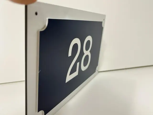 Plăcuță pentru numărul 28, cu fundal închis și ramă deschisă, prezentată în prim-plan.