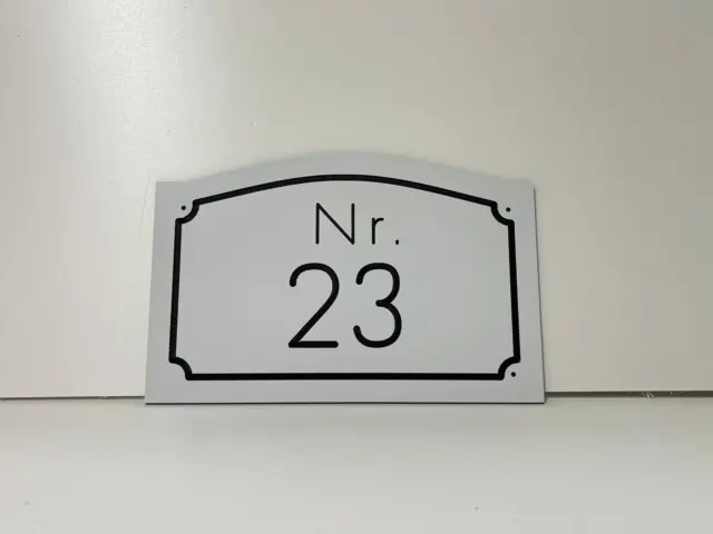 Plăcuță albă pentru număr de locuință, inscripționată „Nr. 23” și conturată cu chenar negru decorativ.