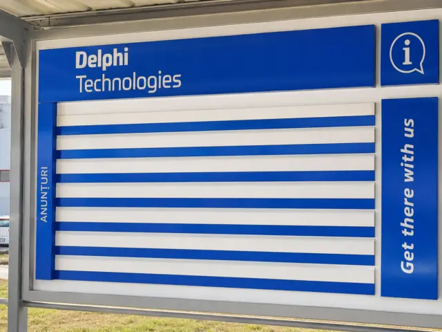 Panou exterior Delphi Technologies, cu spații albastre și albe pentru anunțuri, montat într-un cadru acoperit.