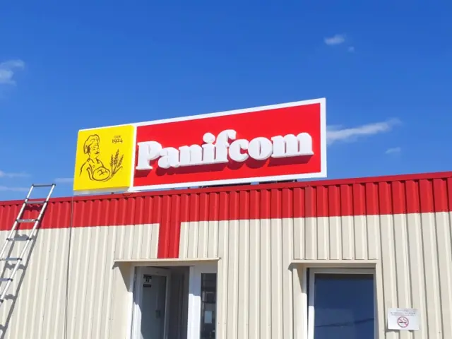 Panou Panifcom cu litere volumetrice albe, montat deasupra fațadei, cu scară alături