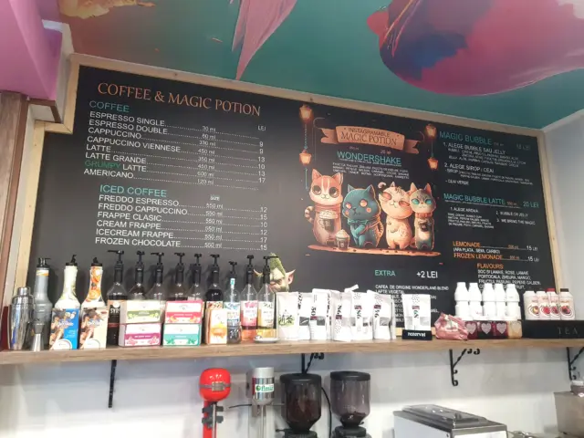 Panou de meniu deasupra tejghelei, cu sortimente de cafea, bubble tea și ilustrații cu pisici.