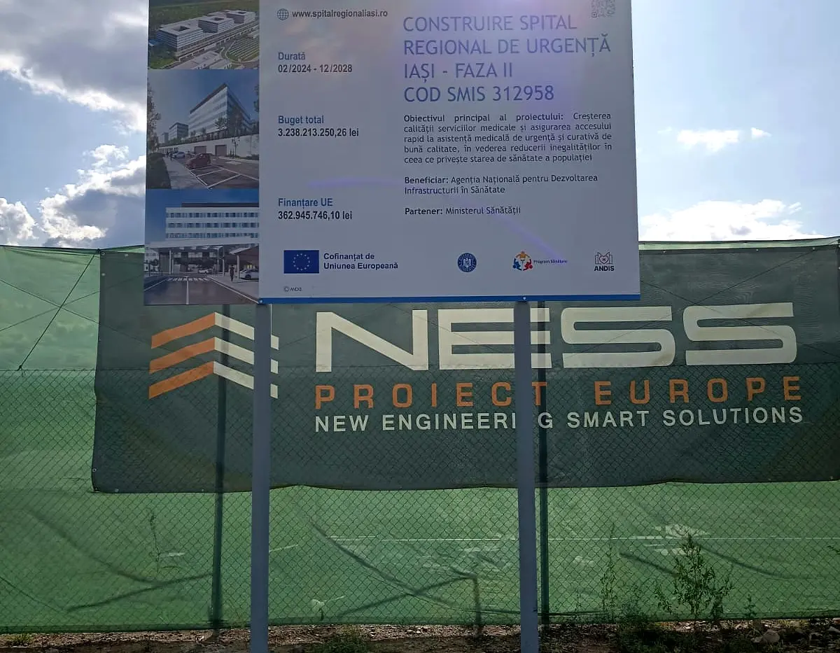Panou informativ exterior pentru construirea Spitalului Regional de Urgență Iași, montat pe doi stâlpi lângă șantier.