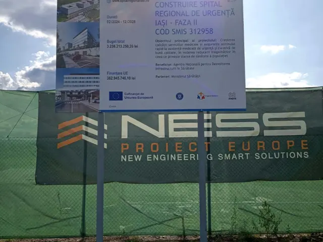 Panou informativ exterior pentru construirea Spitalului Regional de Urgență Iași, montat pe doi stâlpi lângă șantier.