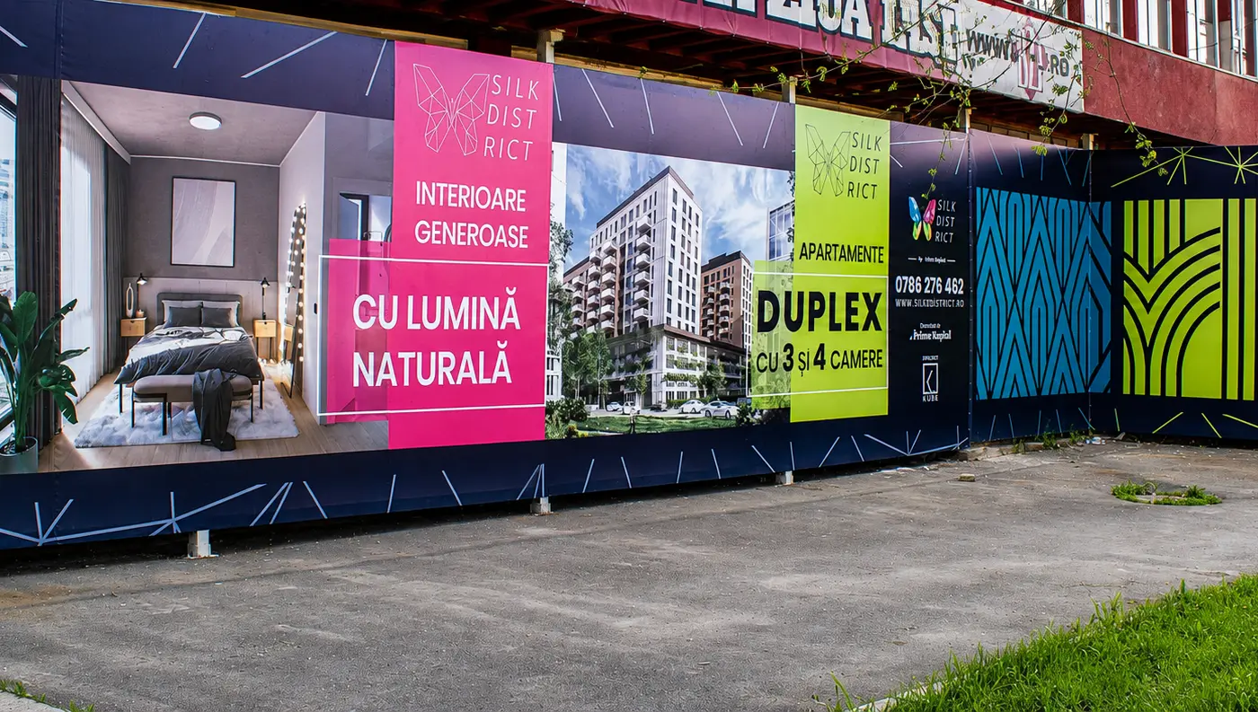 Panou publicitar exterior Silk District, amplasat lângă o clădire, cu randări rezidențiale și elemente grafice colorate.