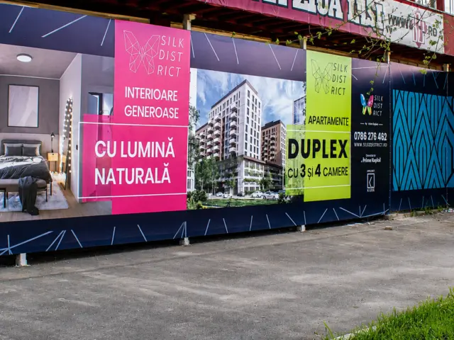 Panou publicitar exterior Silk District, amplasat lângă o clădire, cu randări rezidențiale și elemente grafice colorate.
