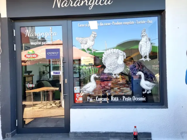 Panou publicitar Narangica deasupra intrării, lângă vitrina decorată cu păsări și produse din carne.