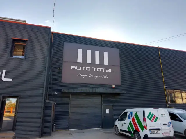 Panou publicitar Auto Total montat pe fațada închisă la culoare a unei clădiri de service auto.