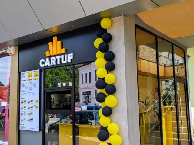 Logo volumetric CARTUF, cu simbol galben, montat pe fațada neagră deasupra intrării.