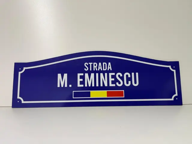 Plăcuță stradală albastră cu contur alb, inscripția „Strada M. Eminescu” și tricolorul României.