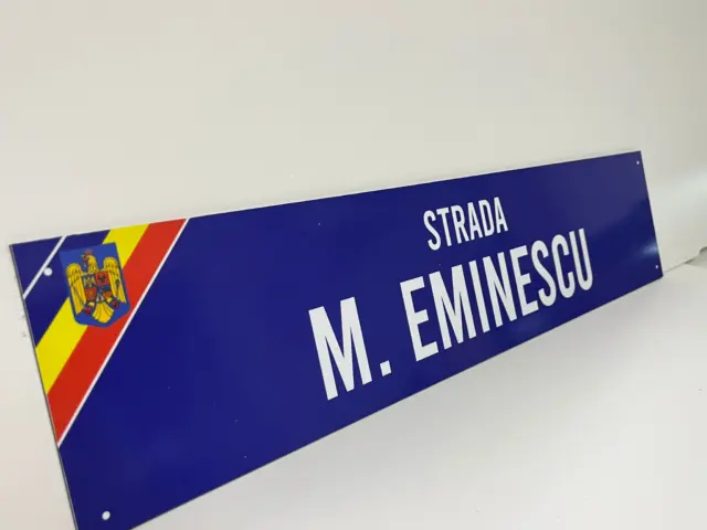 Indicator stradal albastru pentru Strada M. Eminescu, cu text alb, tricolor și stema României.