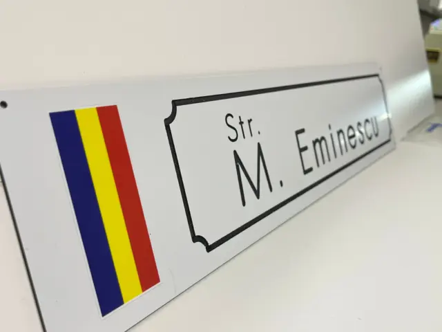 Plăcuță albă pentru Str. M. Eminescu, cu tricolor românesc vertical și chenar negru decorativ, văzută din lateral.