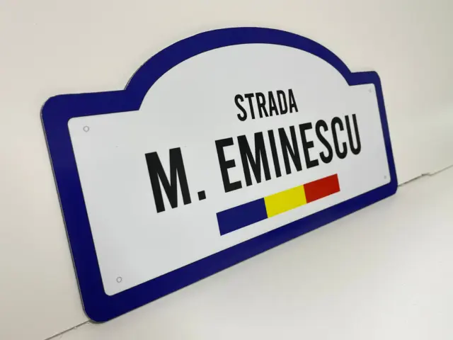 Indicator pentru Strada M. Eminescu, cu fundal alb, chenar albastru arcuit și motiv tricolor.