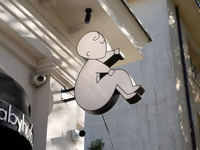 Firmă luminoasă perpendiculară, în forma unui copil care citește, montată pe fațada clădirii.