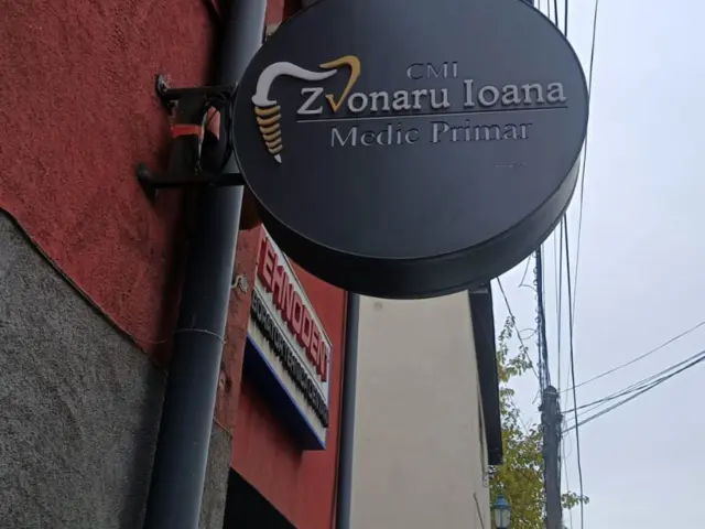 Firmă circulară CMI Zvonaru Ioana, cu simbol dentar, montată perpendicular pe fațada roșie.