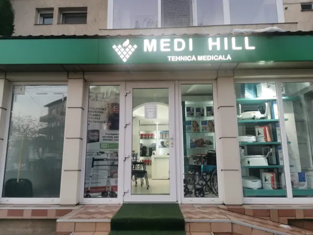 Firmă luminoasă Medi Hill, cu litere albe și simbol, montată deasupra intrării în magazinul de tehnică medicală.