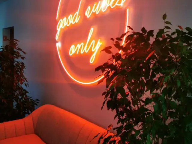 Semn circular din Neon Flex cu mesajul „good vibes only”, montat pe perete lângă o canapea și plante.