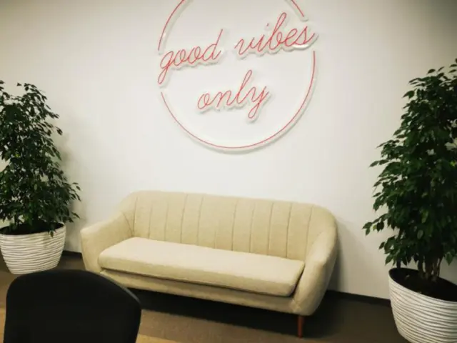 Semn circular roz din Neon Flex, cu mesajul „good vibes only”, montat deasupra unei canapele.