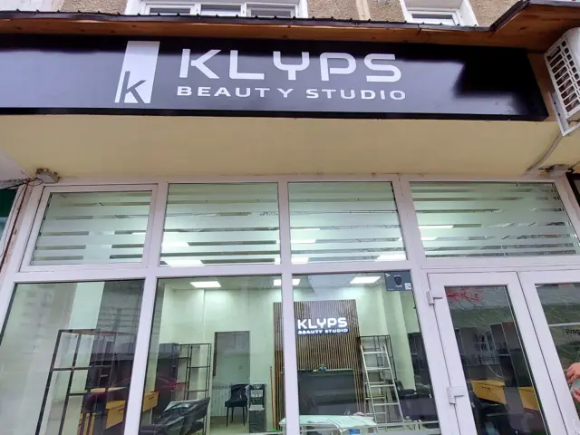 Panou negru KLYPS Beauty Studio, cu litere albe, montat deasupra vitrinei și intrării salonului.