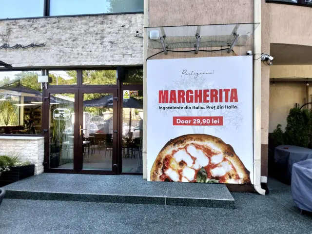 Panou publicitar Partigiano montat lângă intrarea restaurantului, cu pizza Margherita și prețul de 29,90 lei.