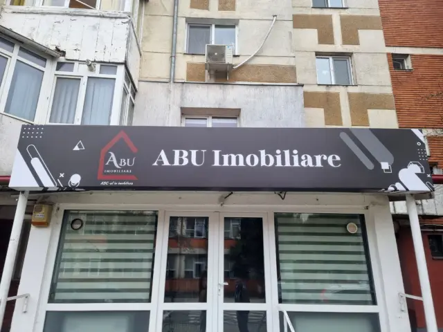 Firma ABU Imobiliare, cu fundal gri și elemente grafice, montată deasupra intrării în sediu.